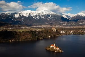 View across Lake Bled to the island church and clifftop castle from Mala Osojnica in spring, Slovenia.