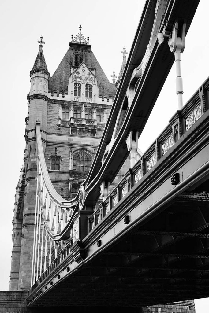 Black and white photo of Tower Bridge in London, England. This is a a combined bascule and suspension bridge, close to the tower of London and crosses the River Thames. It has become a distinctive landmark of the city.