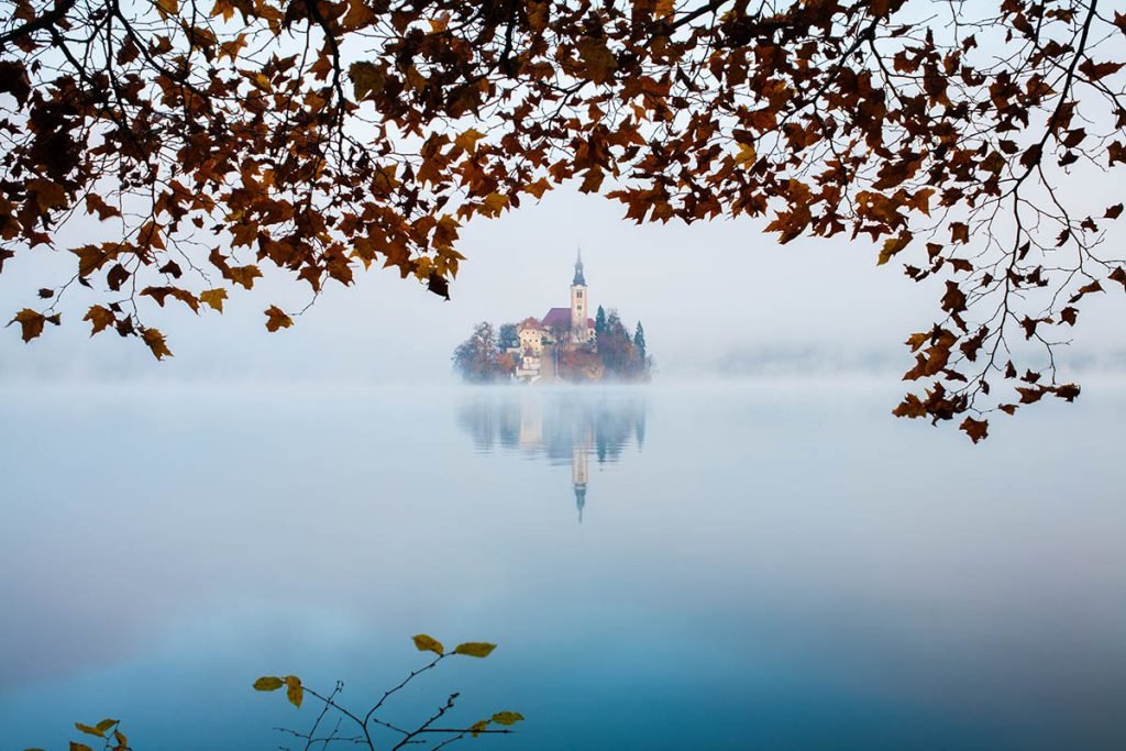 Autumn mist over Lake Bled and the famous island church, framed by trees, Slovenia