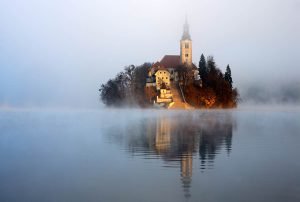 The famous Island church emerging as the morning sun breaks through an icy mist over Lake Bled.
