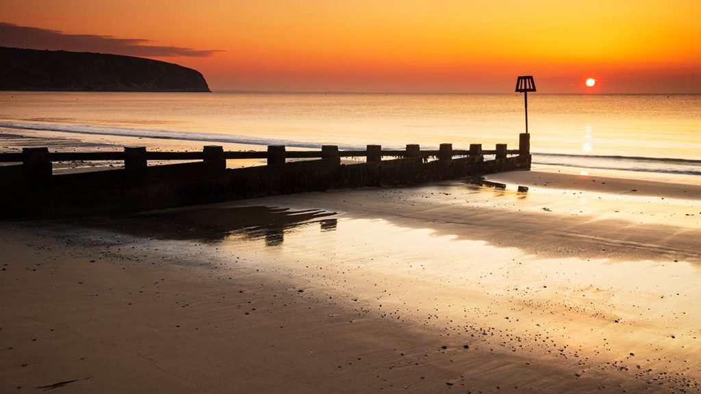 Sun rising Swanage Beach and Groyne, Dorset, England.