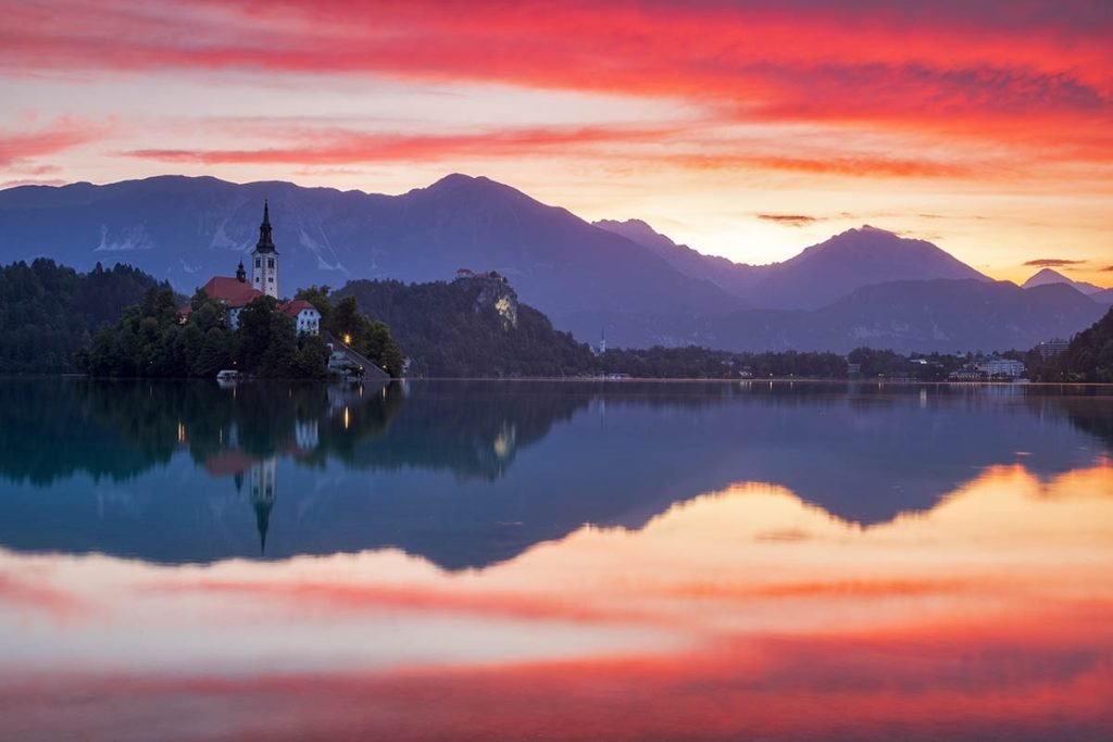 Sun rising over Lake Bled and the island church of the assumption of Mary and castle with the Karavanke mountains in the background, Slovenia.