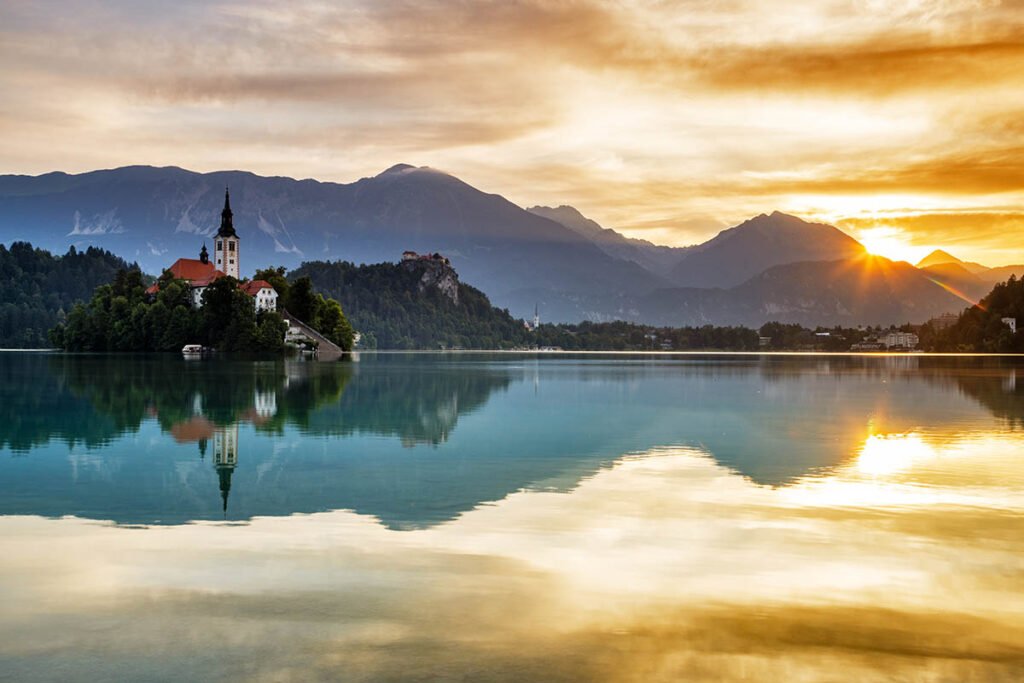 Sun rising over Lake Bled and the island church of the assumption of Mary with the Karavanke mountains in the background, Slovenia.