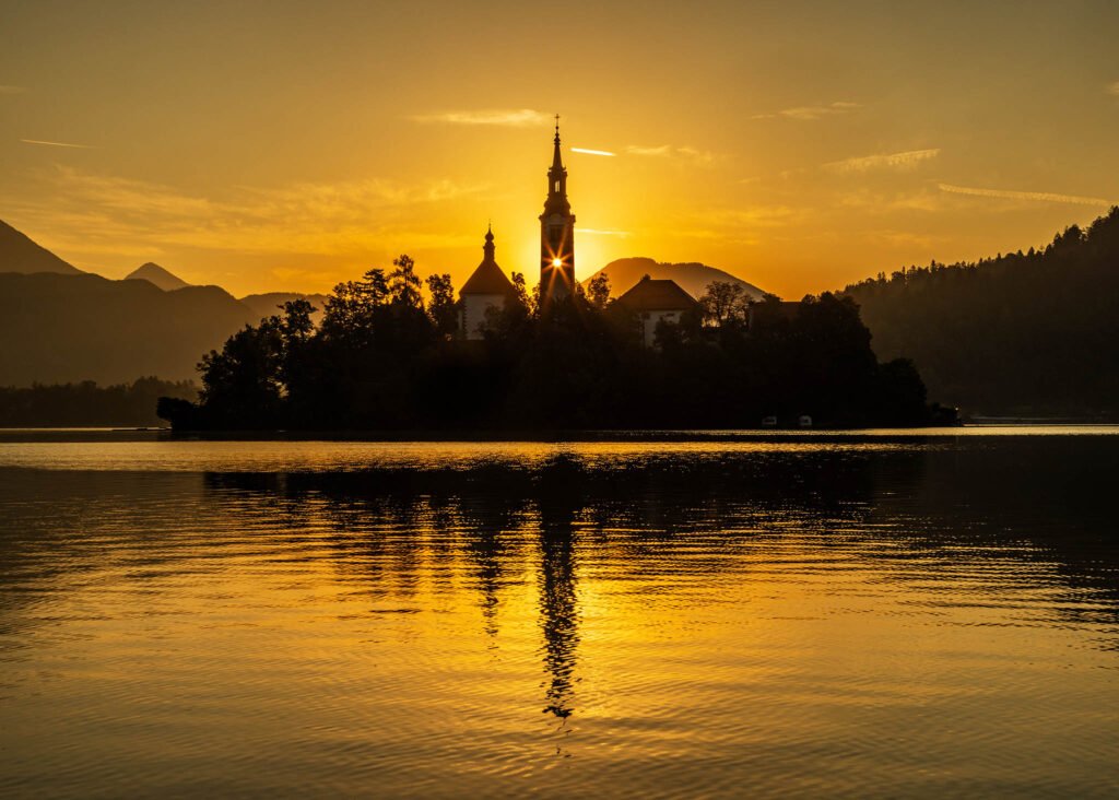 Sun rising over Lake Bled and through the bell tower of the island church of the assumption of Mary, Slovenia.