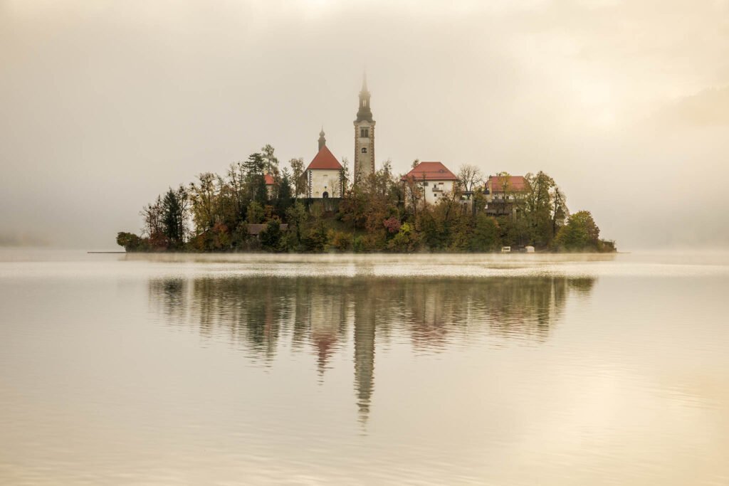 View across misty Lake Bled to the island church in all it's autumn glory, Slovenia.