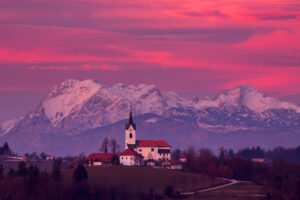 Sunset over the church of Saint Margaret (Sv. Marjeta) in Prezganje in the hills to the east of Ljubljana, Slovenia. The snow covered Kamnik Alps form a beautiful backdrop.
