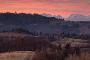 Sunset view across a hill in Prezganje to the church of Saint Nicholas in the village of Jance and the Kamnik Alps to the east of Ljubljana, Slovenia. The shrine on the first hill is to Jesus Christ, built to commemorate the first visit of Pope John Paul the second to Slovenia in 1996.