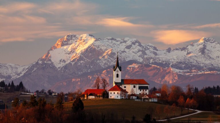 Sunset over the church of Saint Margaret (Sv. Marjeta) in Prezganje in the hills to the east of Ljubljana, Slovenia. The snow covered Kamnik Alps form a beautiful backdrop.