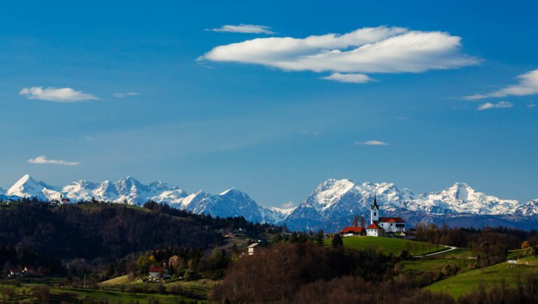 View across to the church of Saint Margaret in Prezganje and the Saint Nicholas and the village of Jance with the Kamnik Alps in the background, in the hilly region to the east of Ljubljana, Slovenia. Seen from Mali Vrh village.